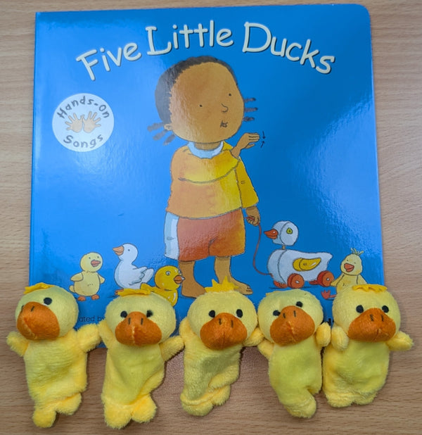 Children's book titled 'Five Little Ducks' with plush duck toys on a wooden surface